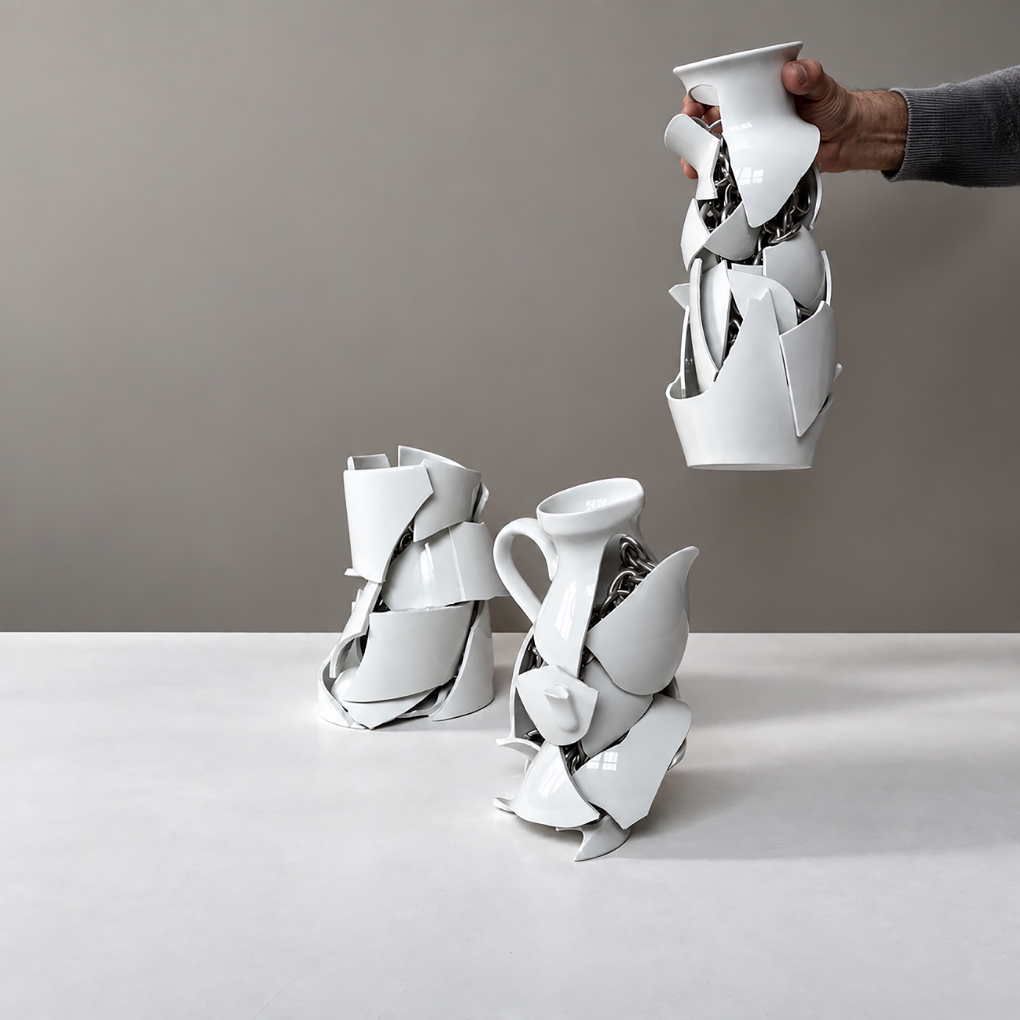 Alberto Gianfreda, Nothing as it seems: mano che solleva una scultura in ceramica frammentata e catene metalliche